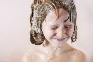 Wall Mural - a little girl washes her hair with shampoo. water pours on her head and she closes her eyes and laug