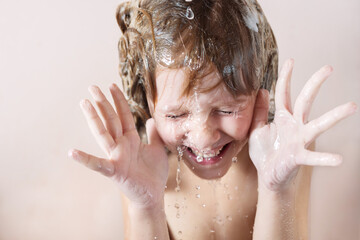Wall Mural - charming little blonde girl washes her hair in the bathroom with foam on her head. water pours, drop