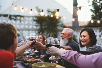 Happy family dining and tasting red wine glasses in barbecue dinner party - People with different ages and ethnicity having fun together