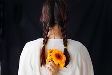 Woman From Behind With Braids And White Shirt, She Holds Orange Flowers Behind Her Back