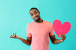 © Carlos David - Portrait of an young man holding pink heart for valentineÕs day love,  looking to side undecided