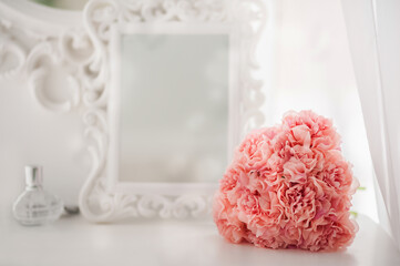 Wall Mural - Pink flowers on the dressing table in the white bedroom. Flowers and perfumes in a bright interior. White boudoir table close up and copy space.