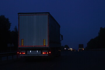 Wall Mural - Semi trailer truck move on dry asphalted night road in dark, back view - intrenational transportation logistics