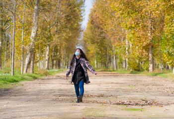 Canvas Print - new normal Autumn walk outdoors - young happy and pretty Asian Korean woman in face mask walking cheerful at beautiful city park in vibrant yellow and orange tree leaves