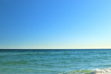 The seascape, a beautiful blank view from the coast of the Gulf of Mexico, calm ocean waters without waves over the horizon converge with a clear blue sky, in the foreground you can see the coast with