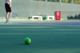 Fototapeta Nowy Jork - close up tennis ball on ground, blurred people playing tennis on tennis court