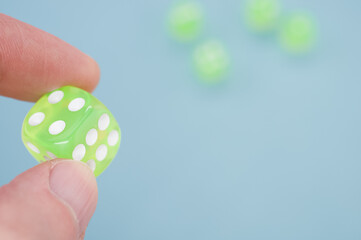 Wall Mural - Closeup of a person's fingers holding a single neon green dice isolated on a blue background