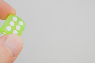 Sticker - Closeup of a person's fingers holding a single neon green dice isolated on a grey background