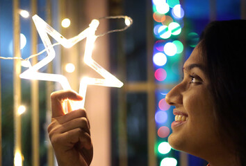 close up portrait of a lady smiling and holding neon star light with bokeh background. Selective focus on face. Diwali festival concept image