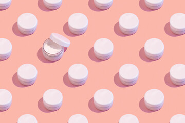 regular pattern of closed jars of cream on a pastel pink background. minimal skin care concept.