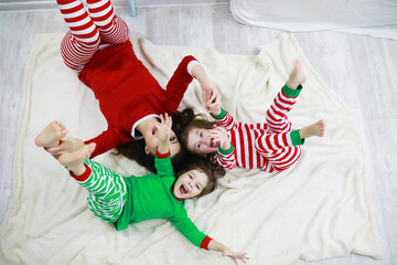 A family in striped pajamas is resting at home. Little children dressed as elves are lying on the sofa. Happy family.