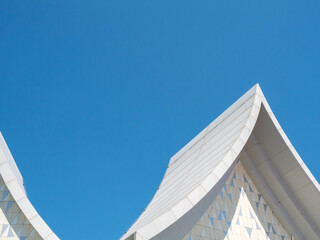 White Thai style roof design in a more modern and minimal style with clear blue sky.