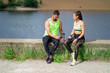 © Georgii - Athletic couple having break during workout sitting with phone and bottle of water outdoor