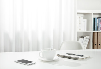 Canvas Print - Closeup of a cup of coffee, a notebook and pen, and a smartphone on a white desk, indoors