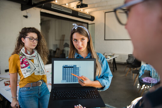 Female designer holding laptop computer and presenting her work to colleagues