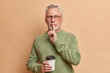 © wayhome.studio  - Shh be silent. Serious bearded grey haired man shows silence gesture asks for secrecy isolated over beige background. Mysterious senior male model looks away and tells secret drinks takeaway coffee