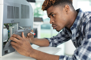 young man repairing photocopier using screwdriver