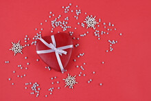 Christmas Gift Box.Merry Christmas And Happy New Year Greeting Card. Xmas Red Gift Box In Form Heart With White Ribbon And Snowflakes On Red Background.Flat Lay With Copy Space.