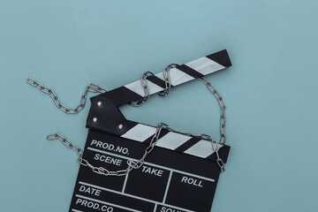 Wall Mural - Movie clapperboard wrapped in steel chain on blue background. Ban on filmmaking. Top view