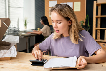 Wall Mural - Young blond pretty female worker of online shop office making caculations