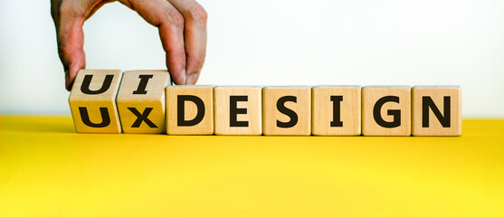 UX design or UI design. Hand turns cubes and changes the words 'UX design' to 'UI design'. Beautiful yellow table, white background. Business concept. Copy space.