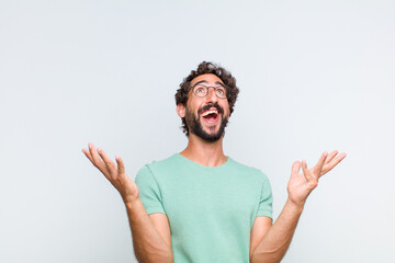 Wall Mural - young bearded man feeling happy, amazed, lucky and surprised, celebrating victory with both hands up in the air