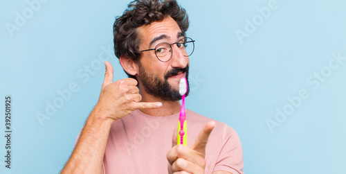 Cuadros en Lienzo young bearded man smiling cheerfully and pointing to camera while making a call