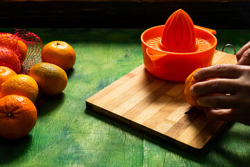 Man's hands making orange juice with a manual juicer on an old wooden background in green tones