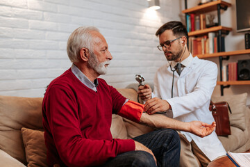 Young handsome doctor visiting examining his senior male patient at his home.