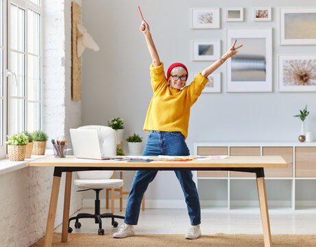 cheerful elderly woman freelancer creative designer in a red hat having fun and dancing in workplace.
