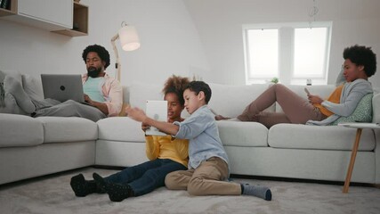 Wall Mural - Everyone has own entertainment. Parents sitting on sofa and using laptop while their children are on the floor and using tablet