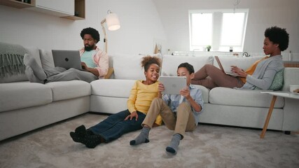 Wall Mural - Parents sitting on sofa and using technology while their children are on the floor and using tablet