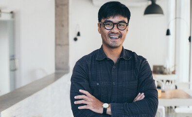 Wall Mural - asian man portrait young male wear eye glasses smiling cheerful look thinking position with perfect clean skin posing on cafe background.fashion people life style concept