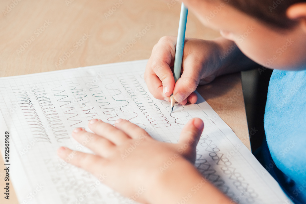 Close up of schoolboy doing writing task. Prewriting practice to prepare hand for write letters. Children education concept - obrazy, fototapety, plakaty 