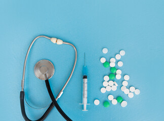 Stethoscope, syringe, many pills on a blue background. Copy space. Flat lay. Coronovirus treatment concept