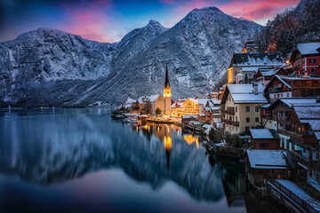 Wall Mural - The little village of Hallstatt, Austria, during winter dusk time with snow, glowing sky in the mountains and warm lights from the houses
