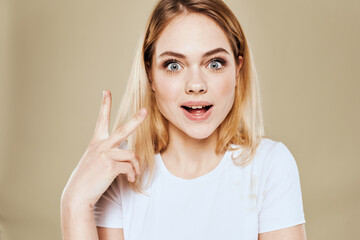 Wall Mural - Cheerful blonde woman in a white T-shirt gestures with her hand emotions beige background