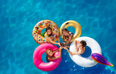 View from above of group of kids drink soda swimming in pool in inflatable toy doughnuts