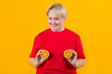 Wall Mural - beautiful young plump female in a red t-shirt on a yellow background with oranges