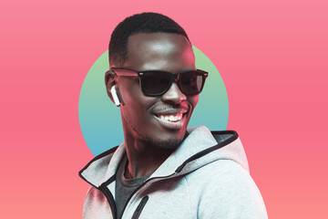 Portrait of young african athlete listening music with earphones, wearing sunglasses isolated on pink background