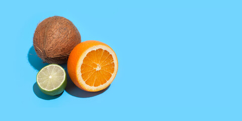 Wall Mural - Fresh juicy orange, coconut and green lime isolated on blue background. Concept of Healthy eating and dieting. Travel and holiday concept. Copy space. Free space for your text