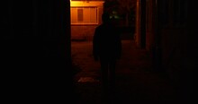 Silhouette Male Figure Walking Through Dimly Lit Back Streets Of City At Night