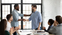 Perfect Job. Friendly African American Boss Or Team Leader Shaking Hand Of Happy Excited Caucasian Employee Manager Worker On Staff Meeting At Boardroom Demonstrating Respect Greeting With Promotion