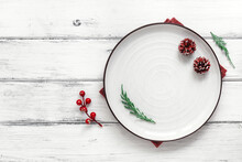Christmas Or New Year's Table Setting. White Empty Plate With Christmas Tree Decorations On A White Wooden Table. Top View, Flat Lay.