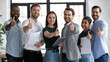 © fizkes - We are glad to recommend. Young modern team of diverse qualified specialists posing for portrait in corporate office looking at camera showing thumb up gesture approving product service able to help