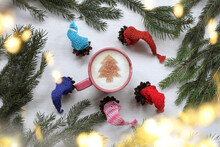 Cones In Multi-colored Caps Around A Cup With Frothy Cappuccino And A Christmas Tree Pattern Top View. Festive Warming Dance Of Forest Dwellers