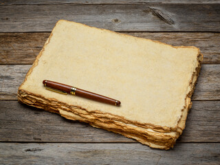 Wall Mural - stack of tan toned heavyweight deckle edge paper sheets with a stylish pen on a rustic weathered wood