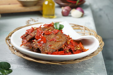 Wall Mural - Indonesia traditional food, Dendeng Balado or beef jerky mix with chili and herbs and spices placed in white plate with lime leaves on top in the corner of the table