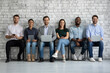 © fizkes - Portrait of young happy people of different gender and ethnicity job applicants business team group of clients posing on chairs in queue with diverse modern gadgets in hands smiling looking at camera