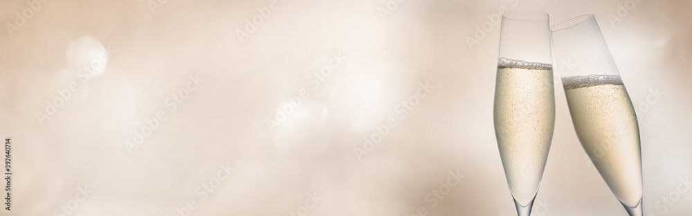 Champagne for festive cheers. Two glasses of sparkling wine in front of tender bright bokeh. Horizontal background for celebrations and invitation cards with space for text. - obrazy, fototapety, plakaty 